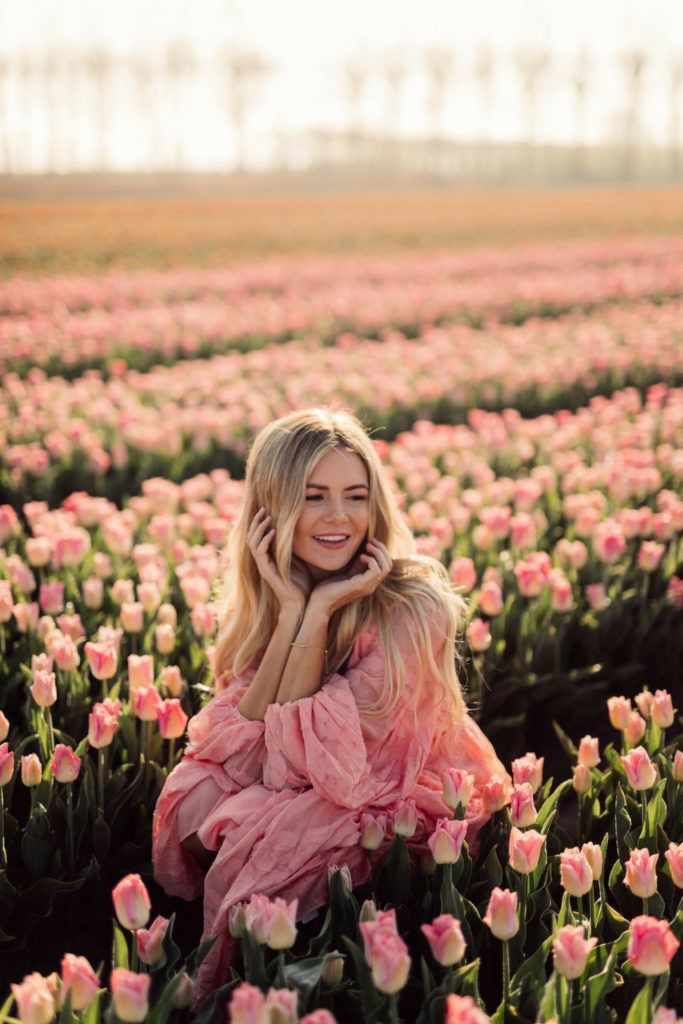 Woman in a pink dress sitting amidst a vibrant field of blooming pink tulips under a soft, sunny sky.