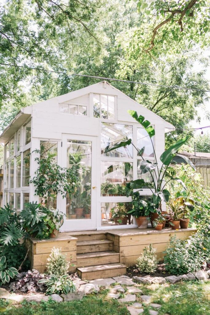 Charming greenhouse surrounded by lush greenery and potted plants in a serene garden setting.