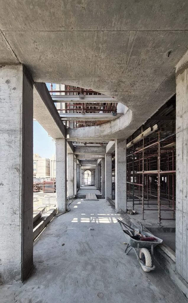 Concrete construction site with scaffolding and wheelbarrow, showing progress in an unfinished building hallway.