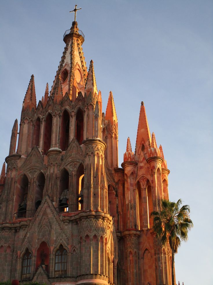 Gothic architecture of a church in warm evening light, with intricate spires and a cross atop the tower.