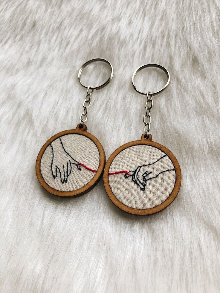 Embroidered keychains with linked hands and red thread on soft fur background. Perfect gift for couples or friends.