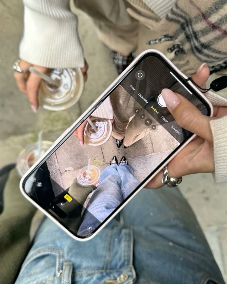 People capturing a stylish overhead photo of iced drinks and fashion outfits with a smartphone.