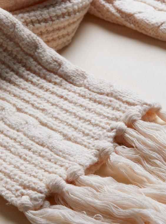 Cozy cream knitted scarf with braided pattern and fringed tassels, perfect for winter warmth and style.