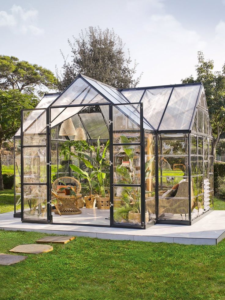 A modern greenhouse with open glass doors filled with lush plants and comfortable seating.