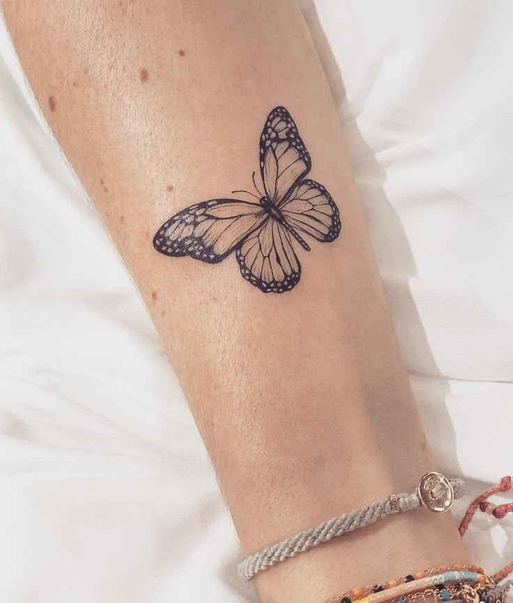 Butterfly tattoo on person's arm, adorned with bracelets, showcasing intricate black and white wing pattern.