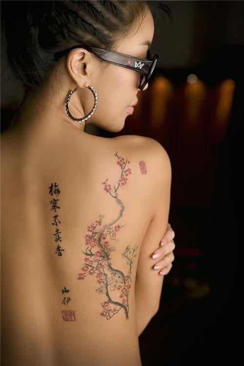 Woman with cherry blossom and Kanji tattoos on back, wearing hoop earrings and sunglasses.