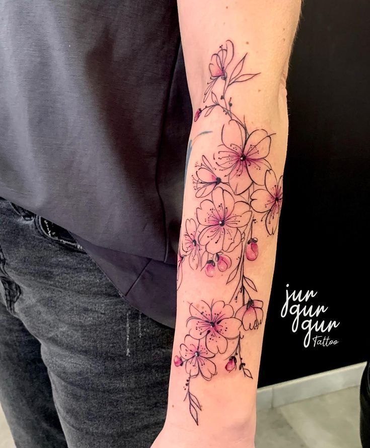 Delicate cherry blossom tattoo on forearm with pink accents, showcasing intricate floral design.