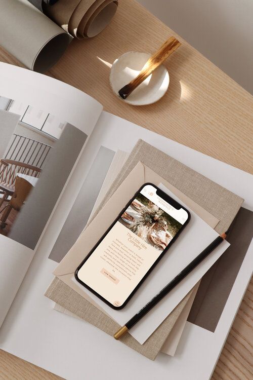 Smartphone displaying a minimalist website, placed on top of magazines and papers with a sleek design.