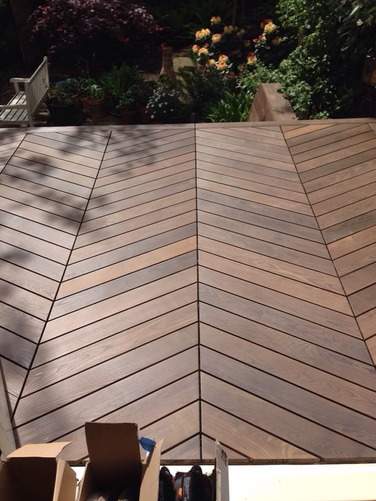 Chevron-patterned wooden deck with garden background in sunlight.