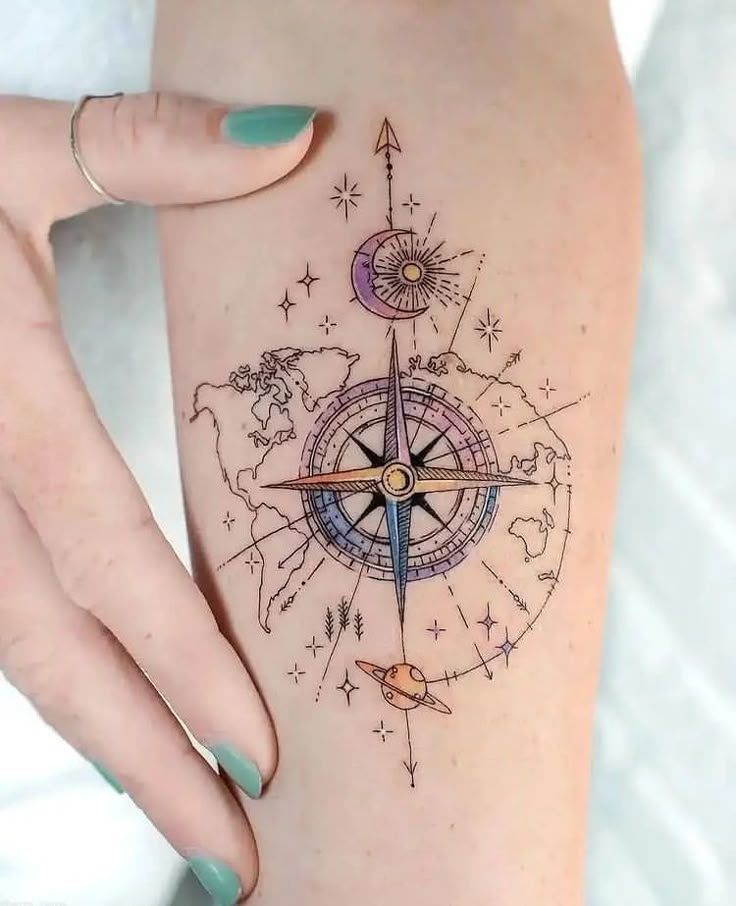 Detailed compass tattoo with world map and celestial elements on arm, designed with pastel shades, held by a hand.