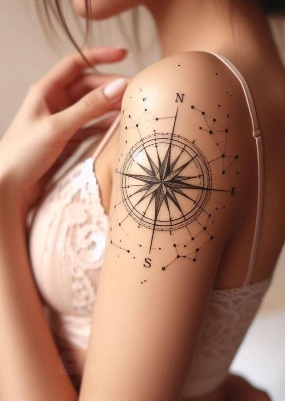 Compass tattoo on a woman's shoulder with starry constellation design, wearing a lace top.