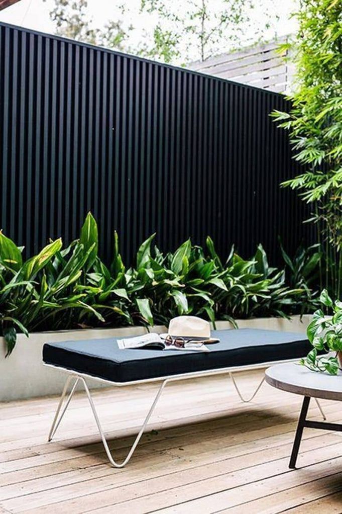 Modern outdoor seating area with black bench, plants, and wooden deck, creating a serene garden retreat.