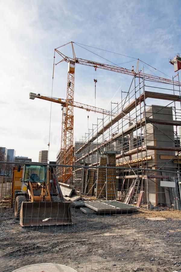 Construction site with cranes and machinery building a structure against a clear blue sky.