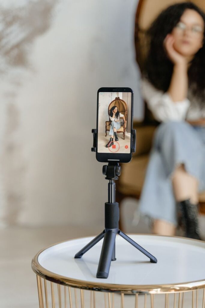 Smartphone on tripod capturing woman sitting on chair, creating content.