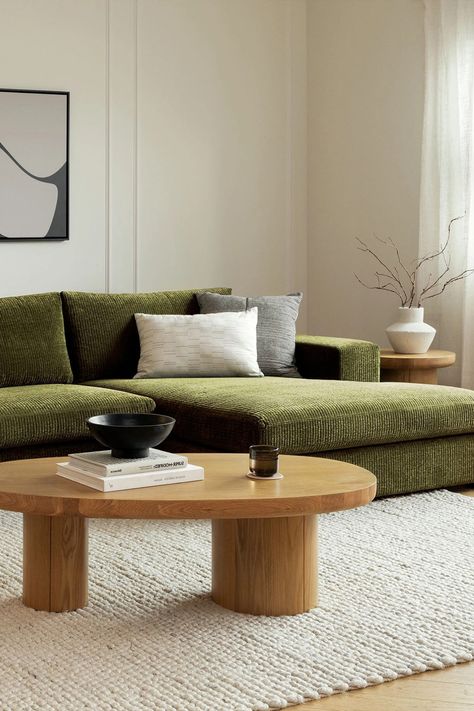 Modern living room with a green sectional sofa, wooden coffee table, abstract art, and cozy decor.