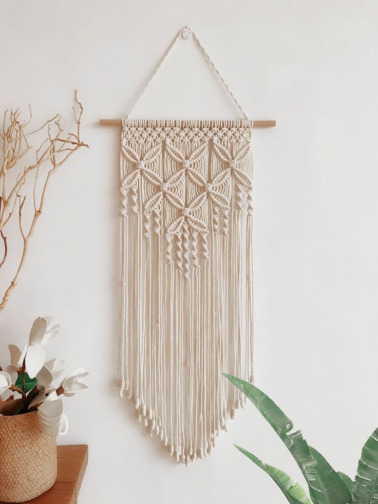 Handmade macramé wall hanging with intricate patterns, perfect for boho home decor. Cream-colored yarn on wood dowel.