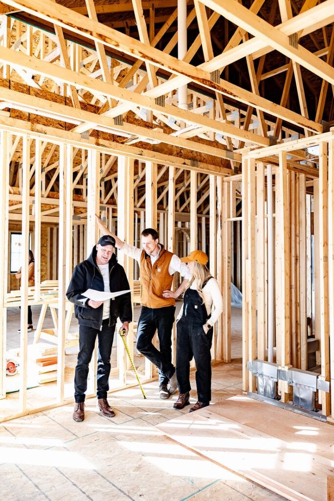 Construction team discussing house framing progress on-site, examining blueprints and measurements.