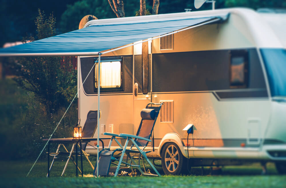 Cozy campsite scene with parked caravan, awning, and chairs illuminated by warm evening light.