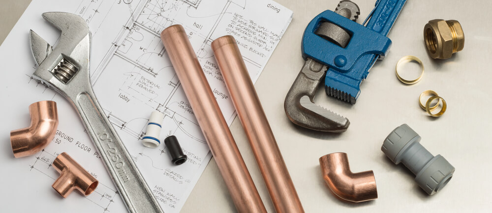 Plumbing tools and copper pipes on construction blueprint, including wrench, fittings, and pipe cutter.