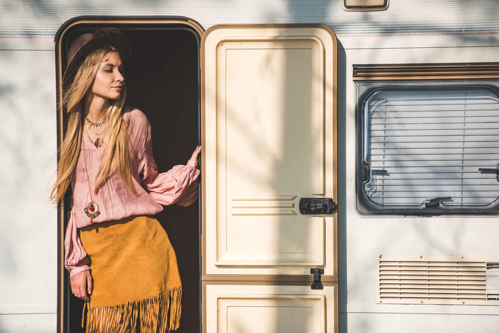 Woman standing in a camper van doorway wearing a boho outfit with a hat.