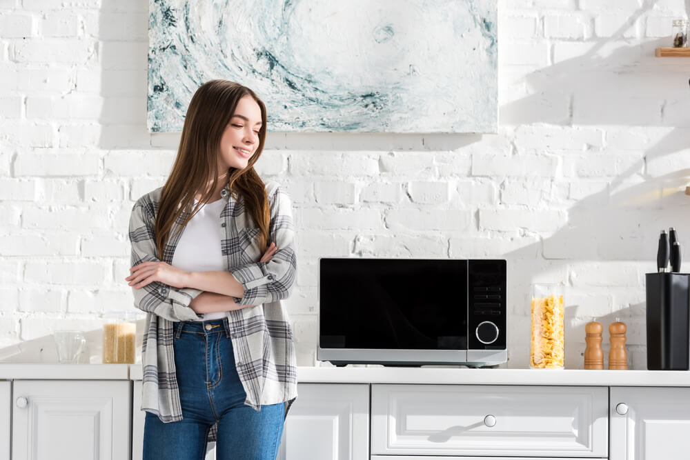 Young woman smiling in a modern kitchen with a microwave on the counter.