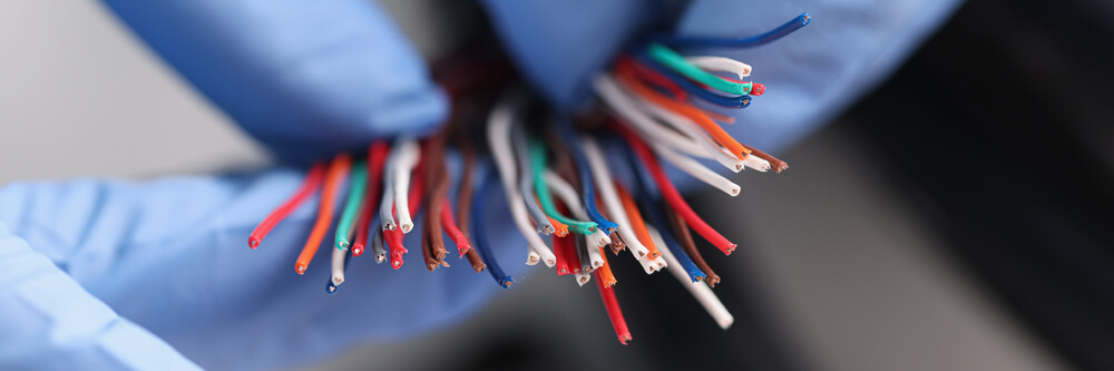 Close-up of gloved hands holding colorful stripped electrical wires, showcasing technology and connection concepts.