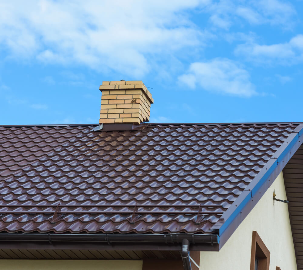 Brown tiled roof with brick chimney against blue sky backdrop.