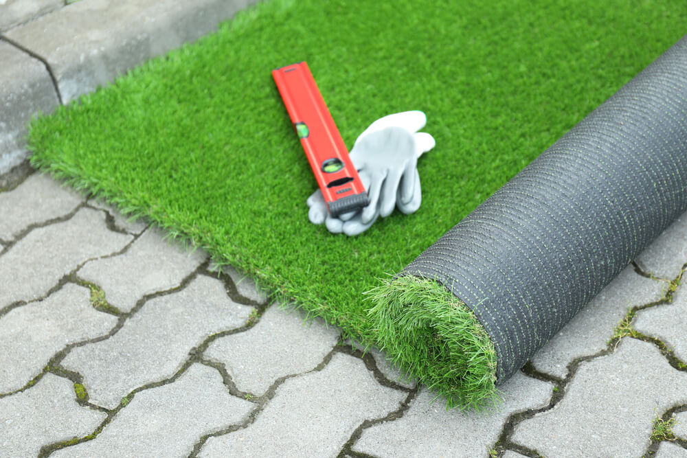 Artificial grass installation tools on patio with a rolled turf, gloves, and a level.