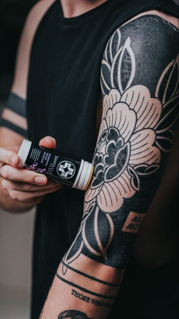 Person applying tattoo balm to arm with floral tattoo design.