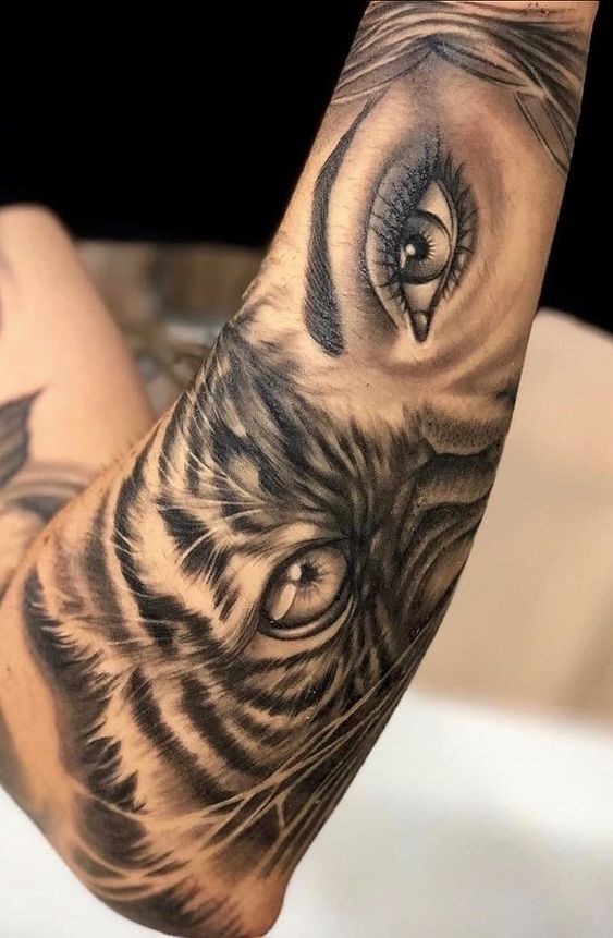 Close-up of a detailed arm tattoo showcasing a woman's eye and a tiger's face in black and gray ink.