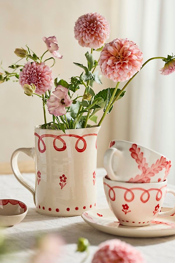 Vintage floral mugs and cups with pink dahlia flowers on a table, showcasing rustic charm and elegance.