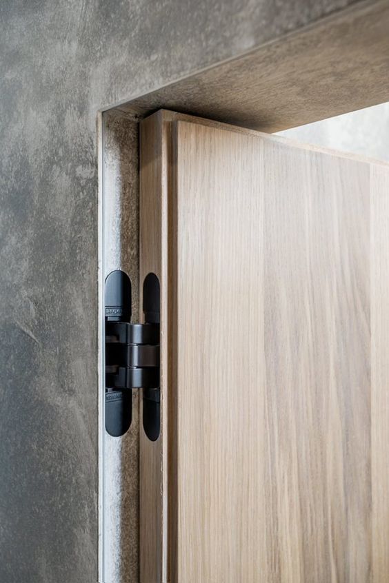 Concealed hinge on a modern wooden door, embedded in a concrete wall, showcasing minimalistic design elements.