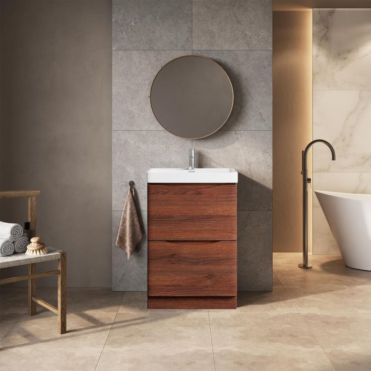 Modern bathroom with wood vanity, round mirror, freestanding bathtub, and towel rack on marble and stone tile flooring.