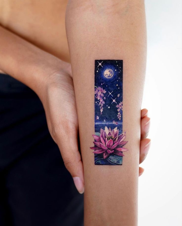 Arm tattoo featuring a pink lotus under a starry night sky with a full moon and purple flowers.