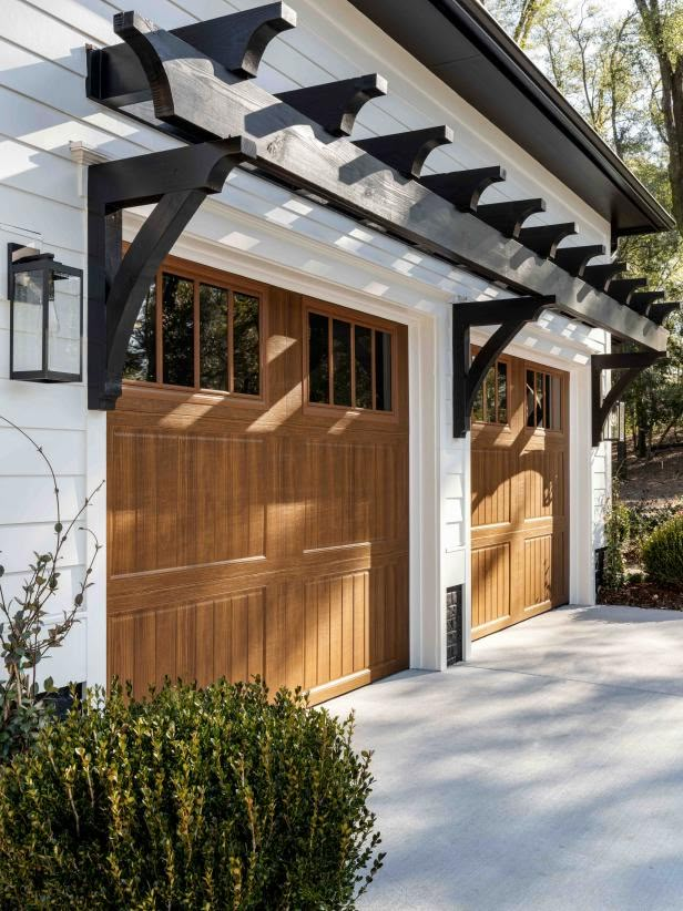 Modern house with wooden garage doors and white exterior, featuring black trim and decorative overhang accents.