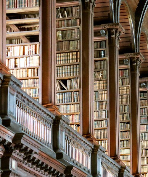 Historic library with tall wooden bookshelves filled with old books and intricate architectural details.