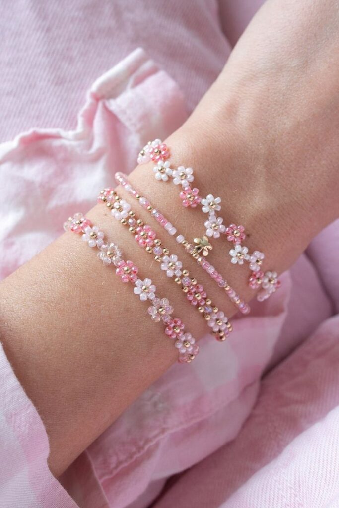 Hand wearing pink and white floral beaded bracelets against a soft pink fabric background.