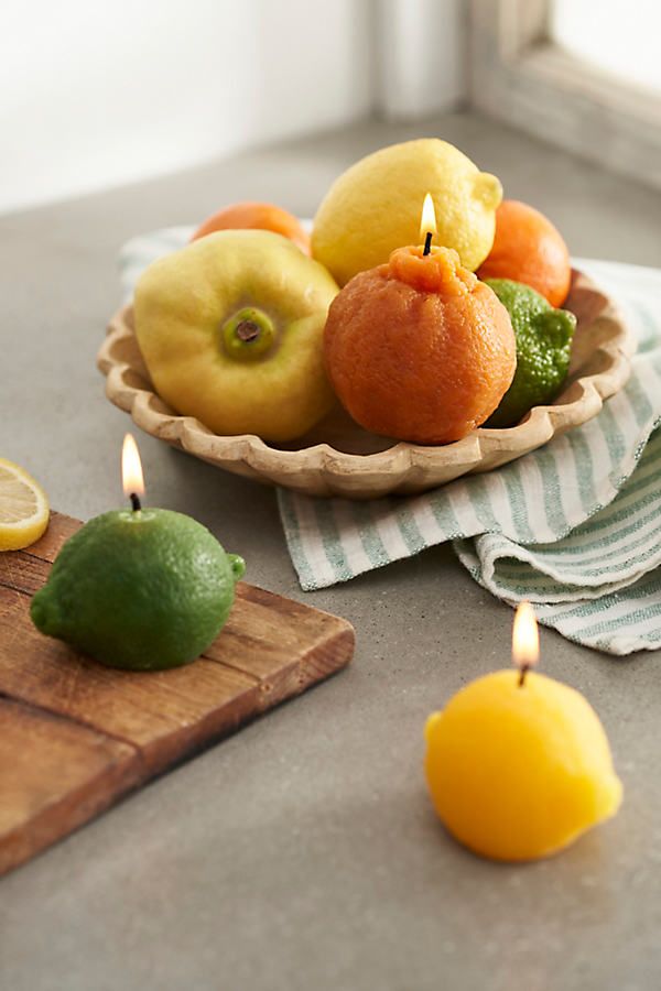 Fruit-shaped candles lit on a wooden tray and table, featuring lemon, lime, and orange designs for cozy home decor ambiance.