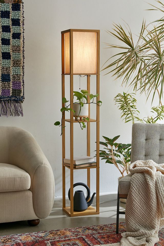 Lamps Design 3 Modern wooden floor lamp with shelves, holding a plant, book, and watering can, beside cozy living room furniture. | Sky Rye Design Modern wooden floor lamp with shelves, holding a plant, book, and watering can, beside cozy living room furniture.