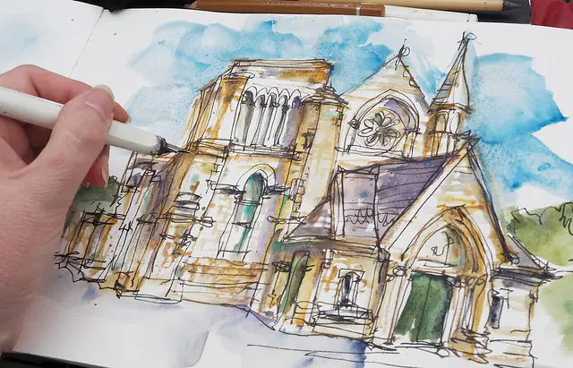 Sketch of a historic cathedral in watercolor with an artist’s hand adding details in a notebook.