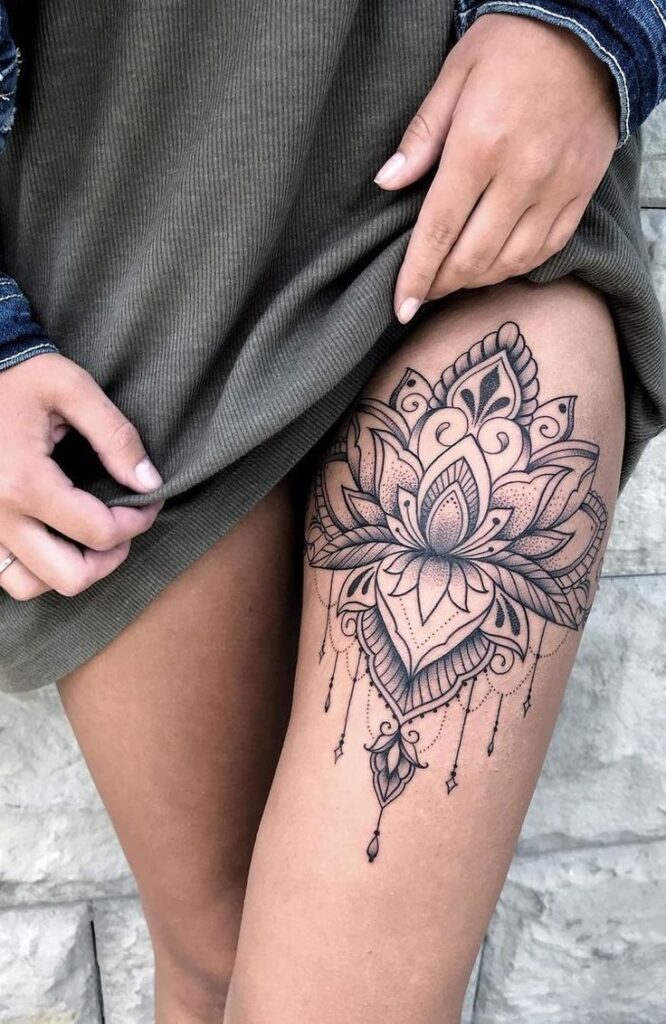 Intricate lotus tattoo design on thigh, featuring geometric patterns and delicate dangling embellishments.