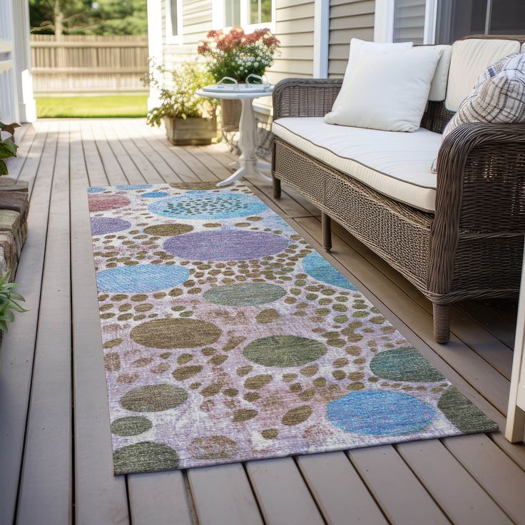 Colorful outdoor rug with circular patterns on a patio, near a wicker sofa and potted plants.