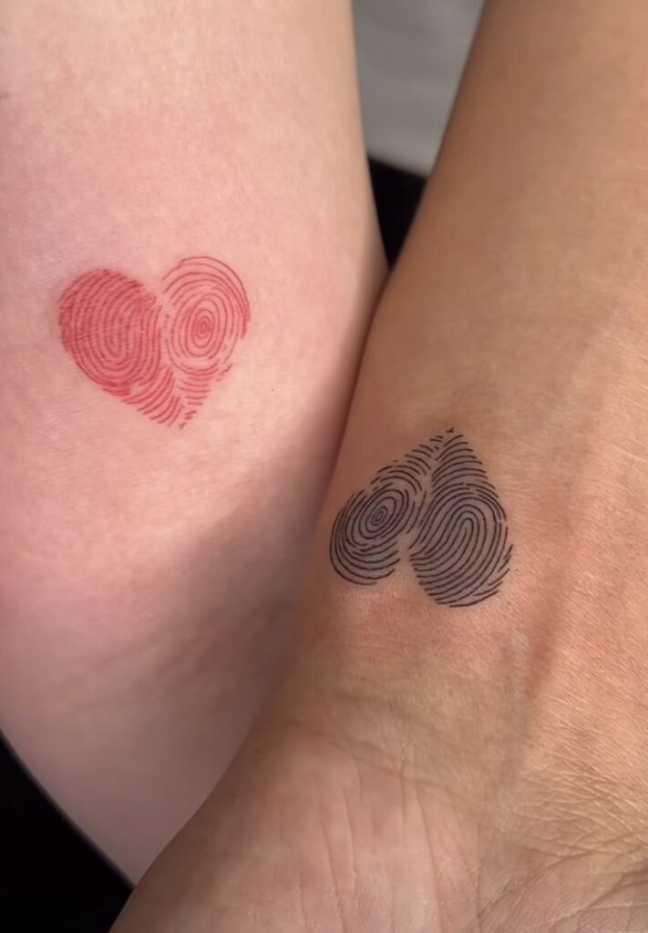 Heart-shaped fingerprint tattoos on skin, one red, one black, symbolizing love and individuality.