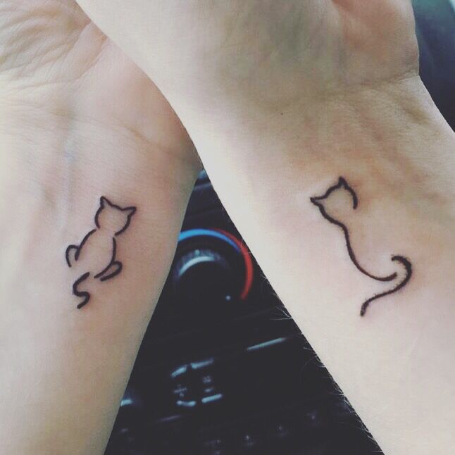 Minimalist cat tattoos on wrists, symbolizing connection and friendship, with a car dashboard in the background.