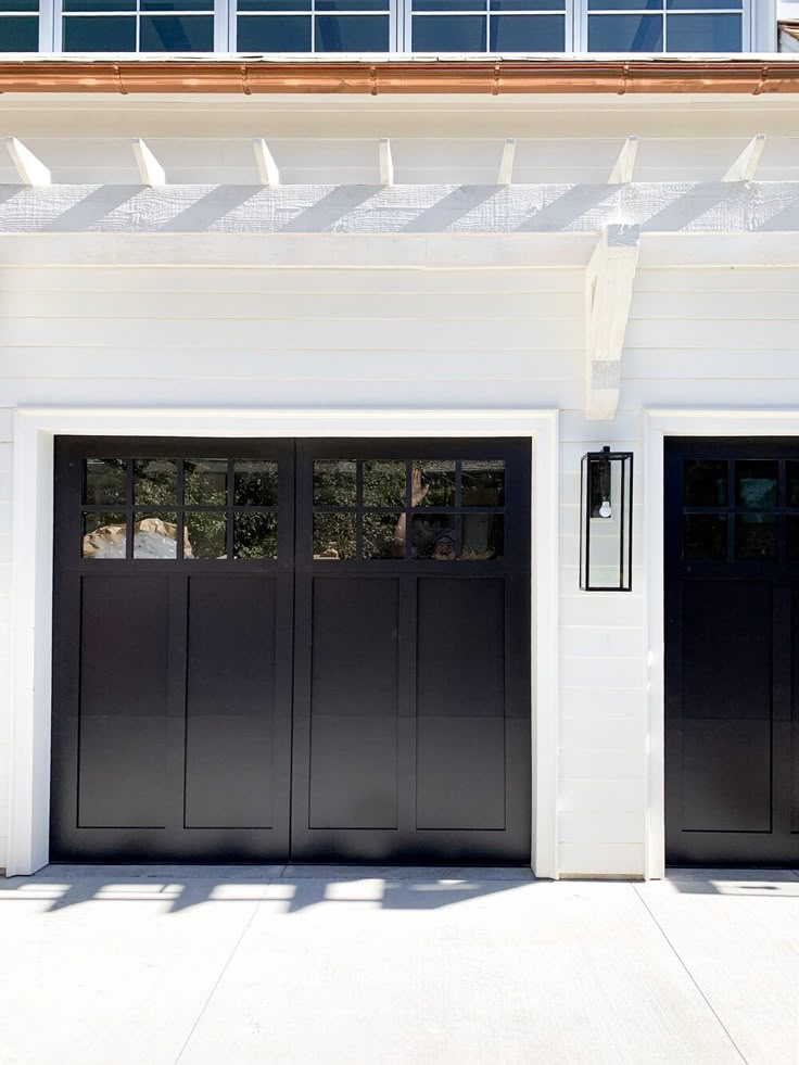 Modern black garage door with white trim and sleek exterior light fixture.