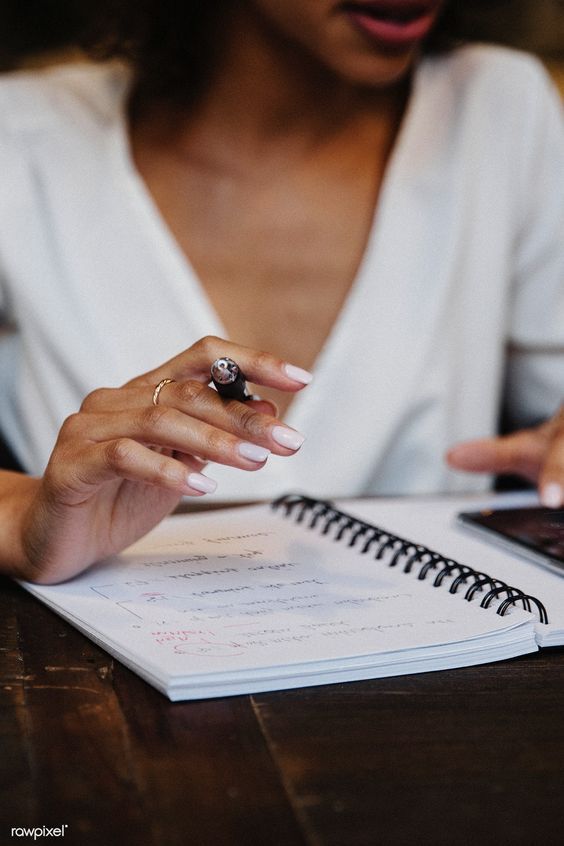 Woman taking notes in a spiral notebook, holding a pen, focused on writing in a casual setting.