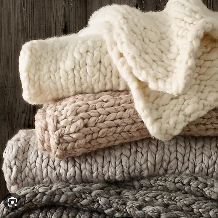 Stack of cozy, chunky knit blankets in soft neutral tones, perfect for adding warmth and texture to any space.