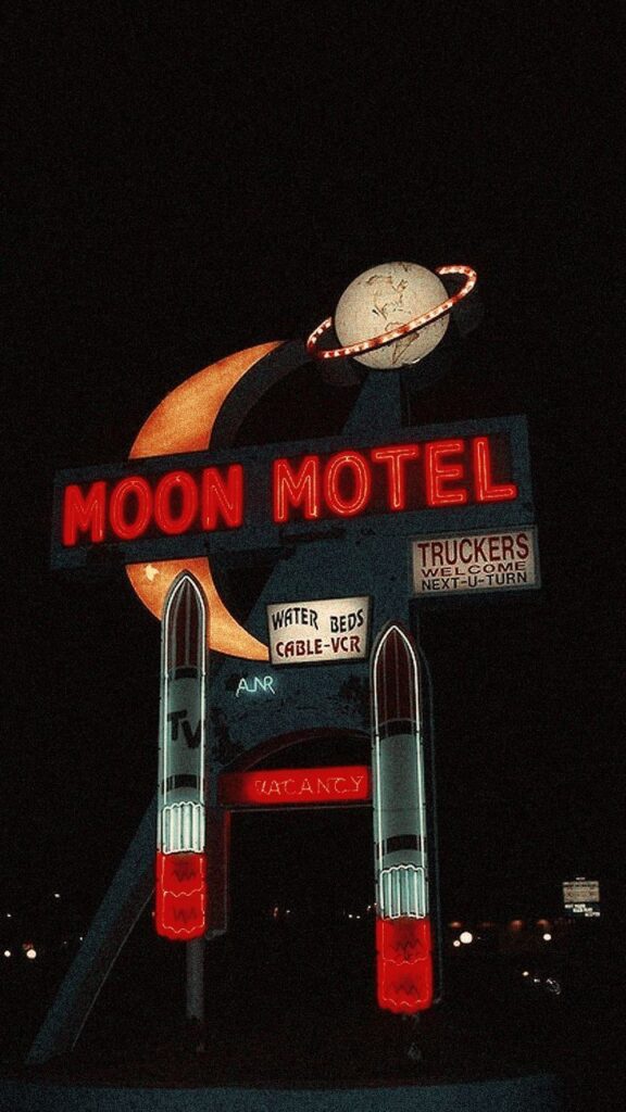 Vintage neon Moon Motel sign with rockets and planet motif lit up at night.