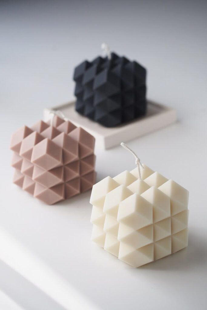 Geometric decorative candles in black, beige, and white on a minimalist surface.