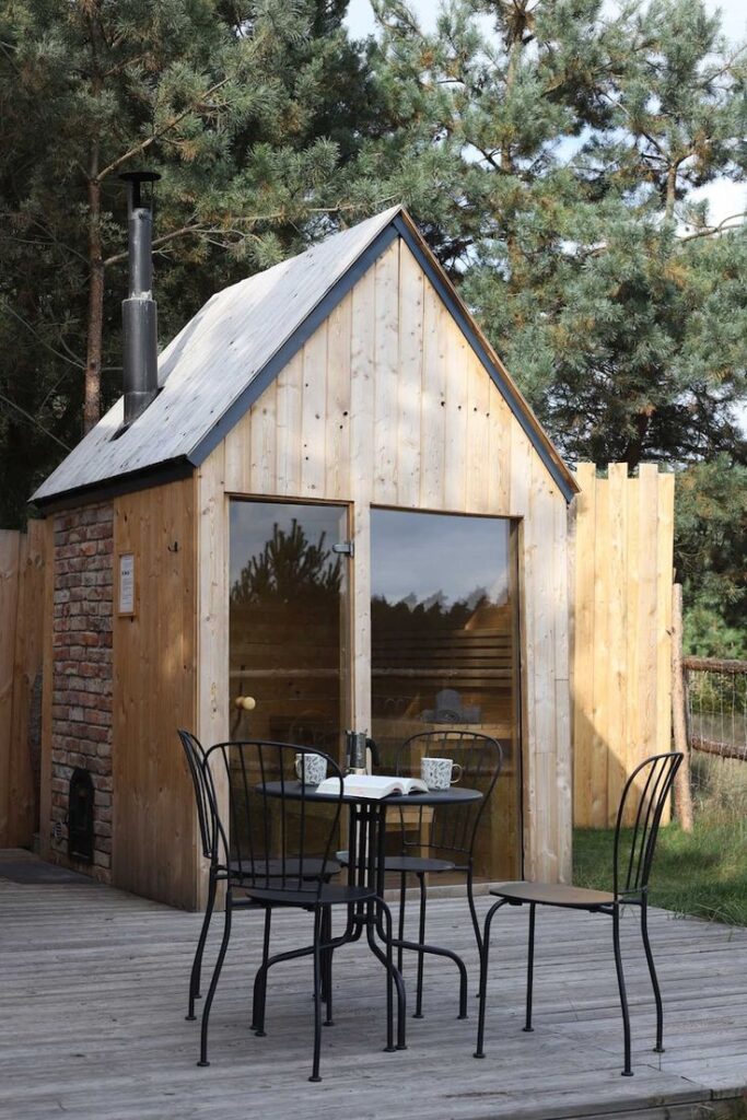 Cozy wooden cabin with outdoor seating, nestled among pine trees, perfect for a relaxing retreat.